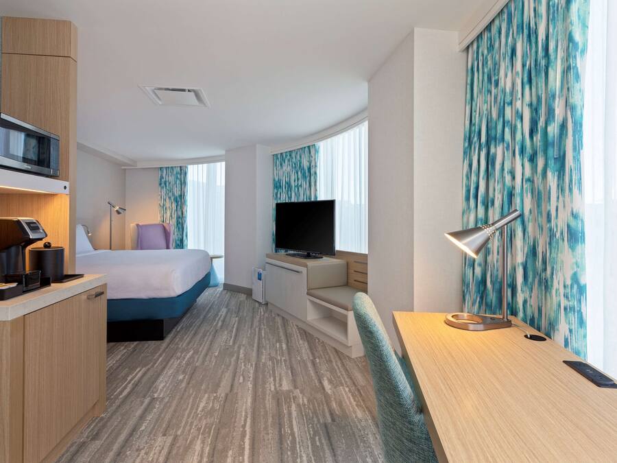 A hotel room with a bed, a desk, a TV, a microwave, and a small kitchenette.