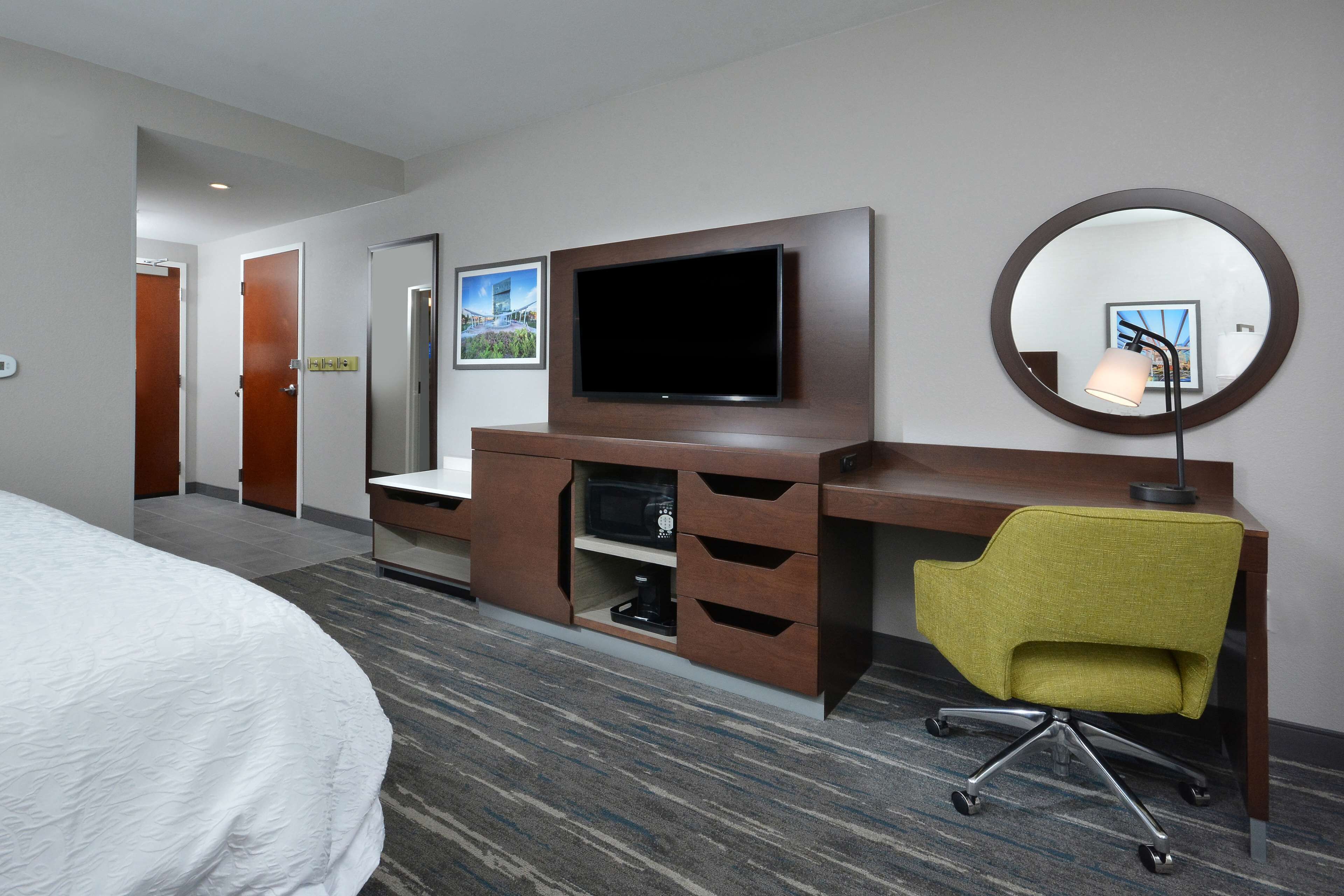 A hotel room with a bed, a desk with a chair, a television, and a mirror.