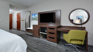 A hotel room with a bed, a desk with a chair, a television, and a mirror.