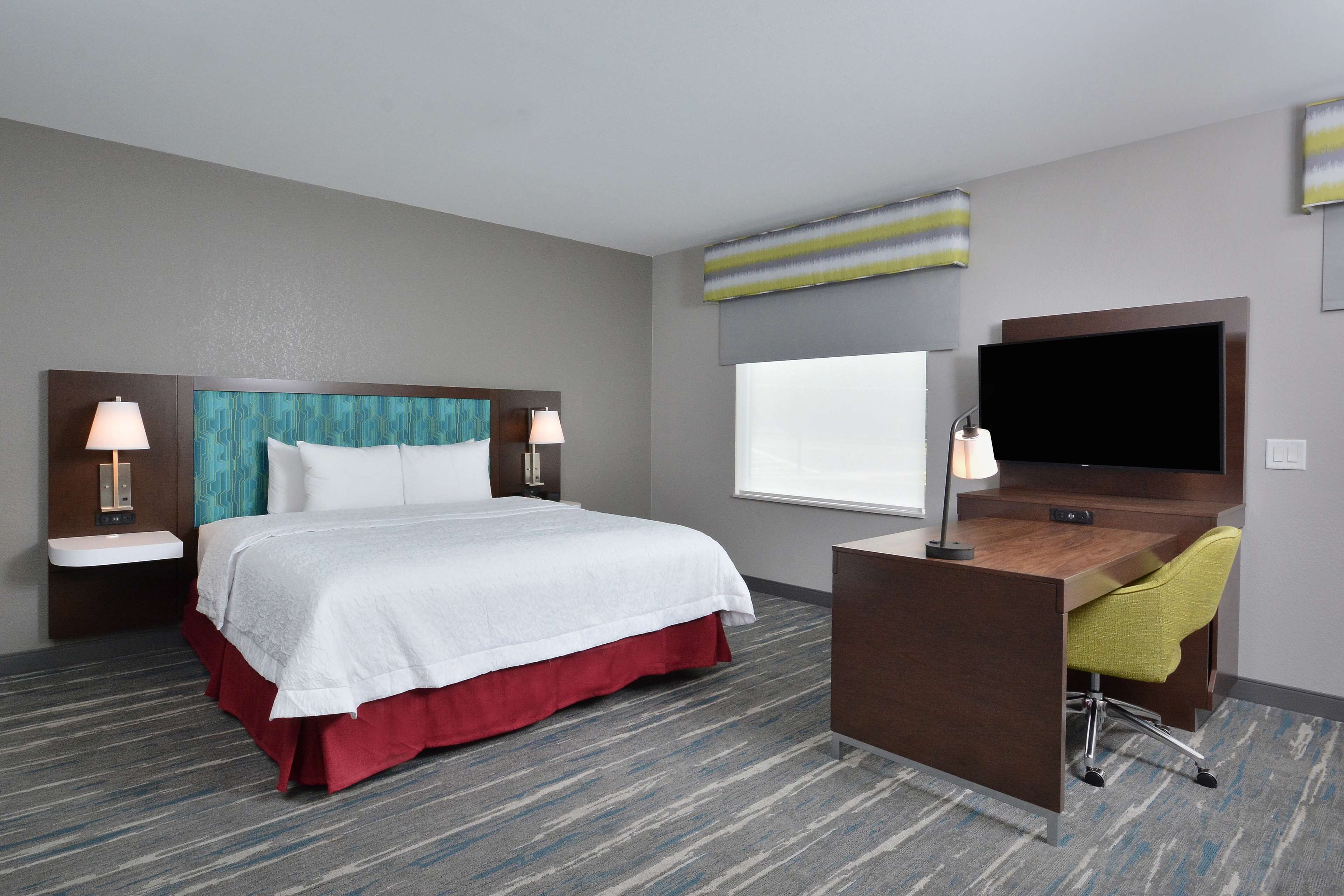 Une chambre d’hôtel avec un lit, un bureau, une chaise, une télévision et une fenêtre.