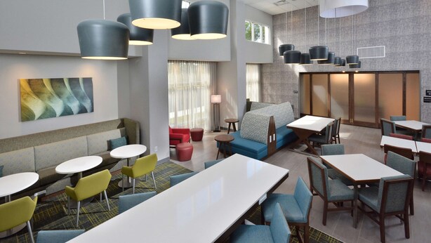 A modern hotel lobby with seating areas, tables, and hanging pendant lights. - Hampton Inn & Suites by HIlton Charlotte North I 485 (Charlotte)