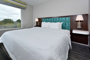 Ett hotellrum med en stor säng, två sängbord med lampor, utsikt över träd genom ett fönster och en sänggavel med mönster.