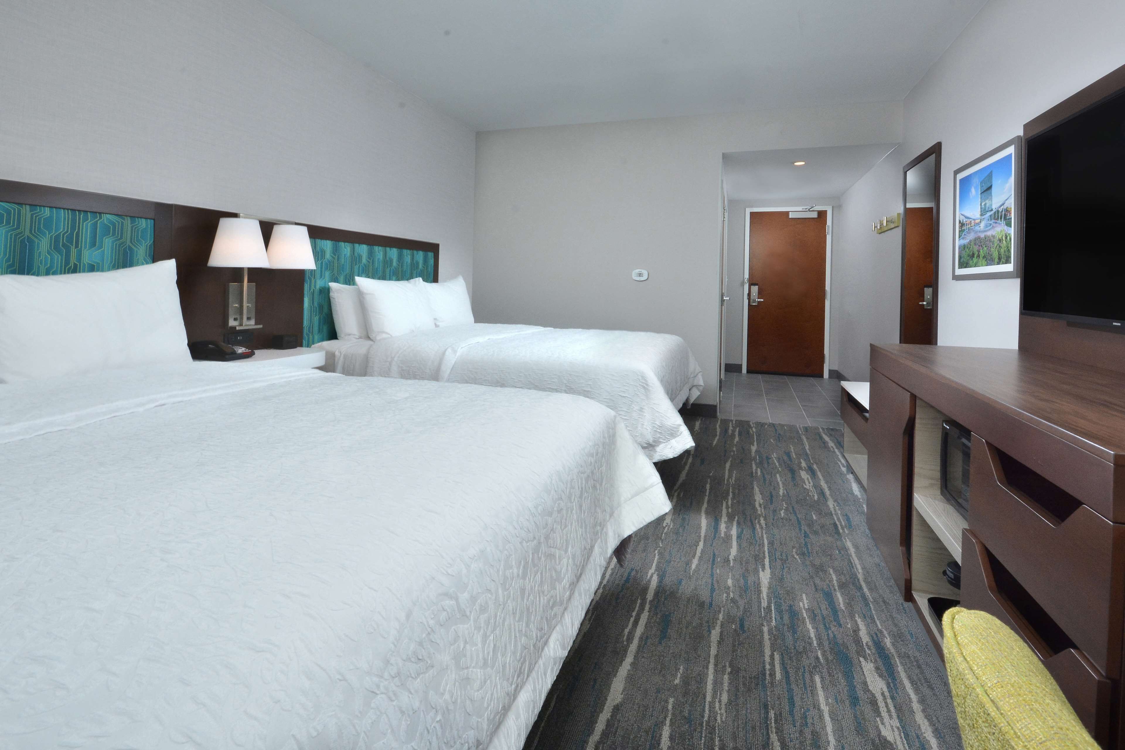 A hotel room with two beds, a desk, a TV, and a door leading to another room.