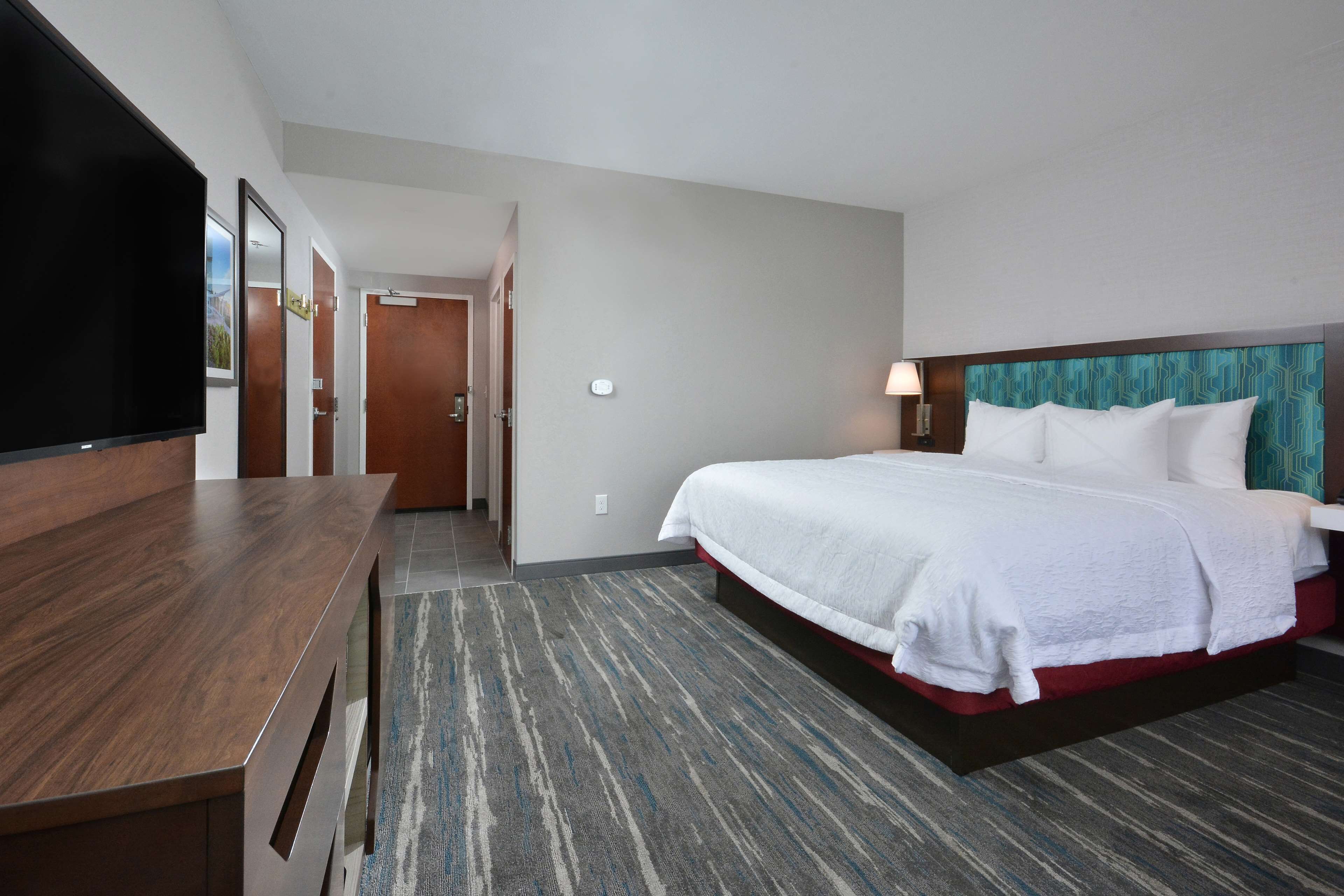 A hotel room with a bed, a TV, a desk, and a carpeted floor.