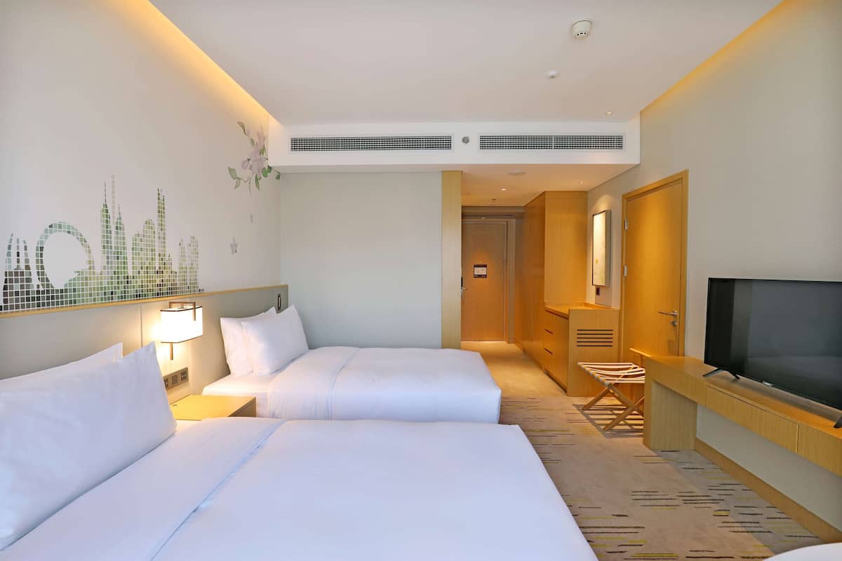 Habitación de hotel con dos camas, televisión, escritorio y un mural en la pared.