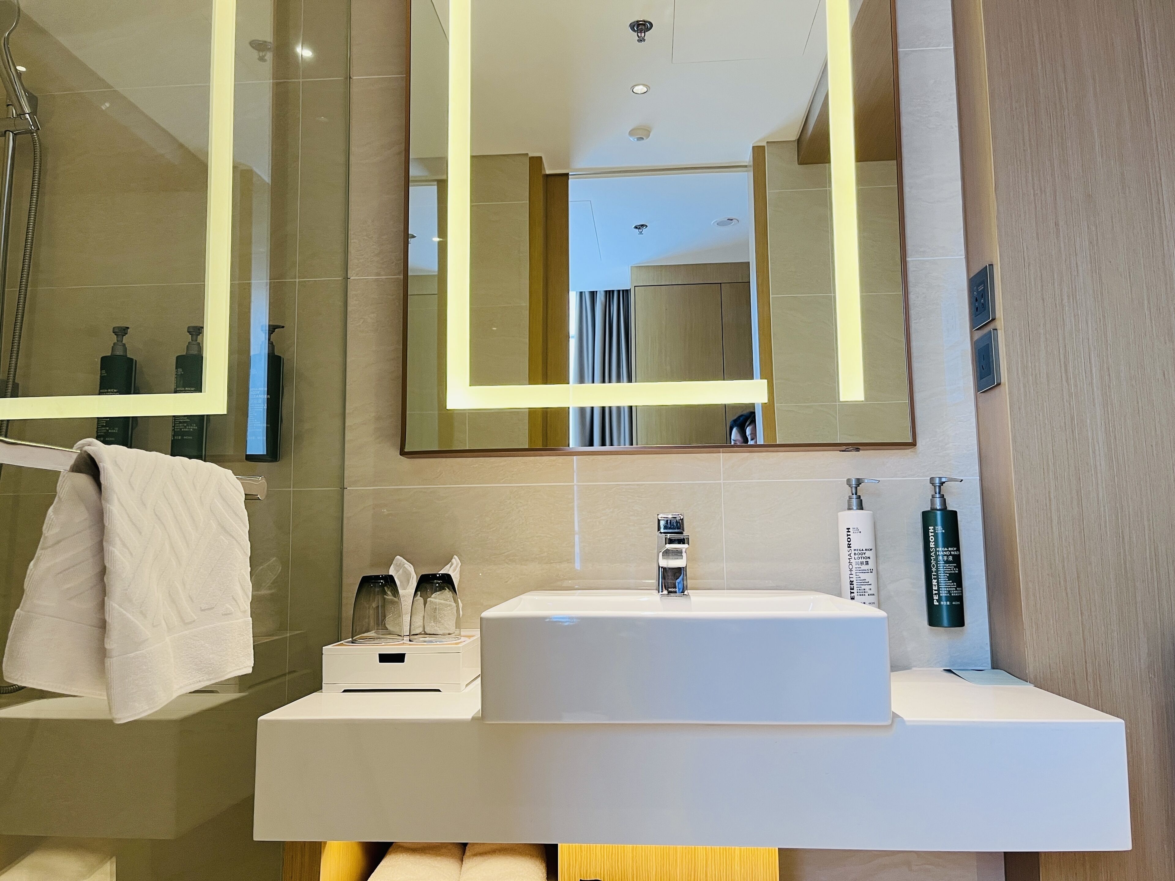 Un baño moderno con un espejo grande, un lavamanos blanco y una ducha.