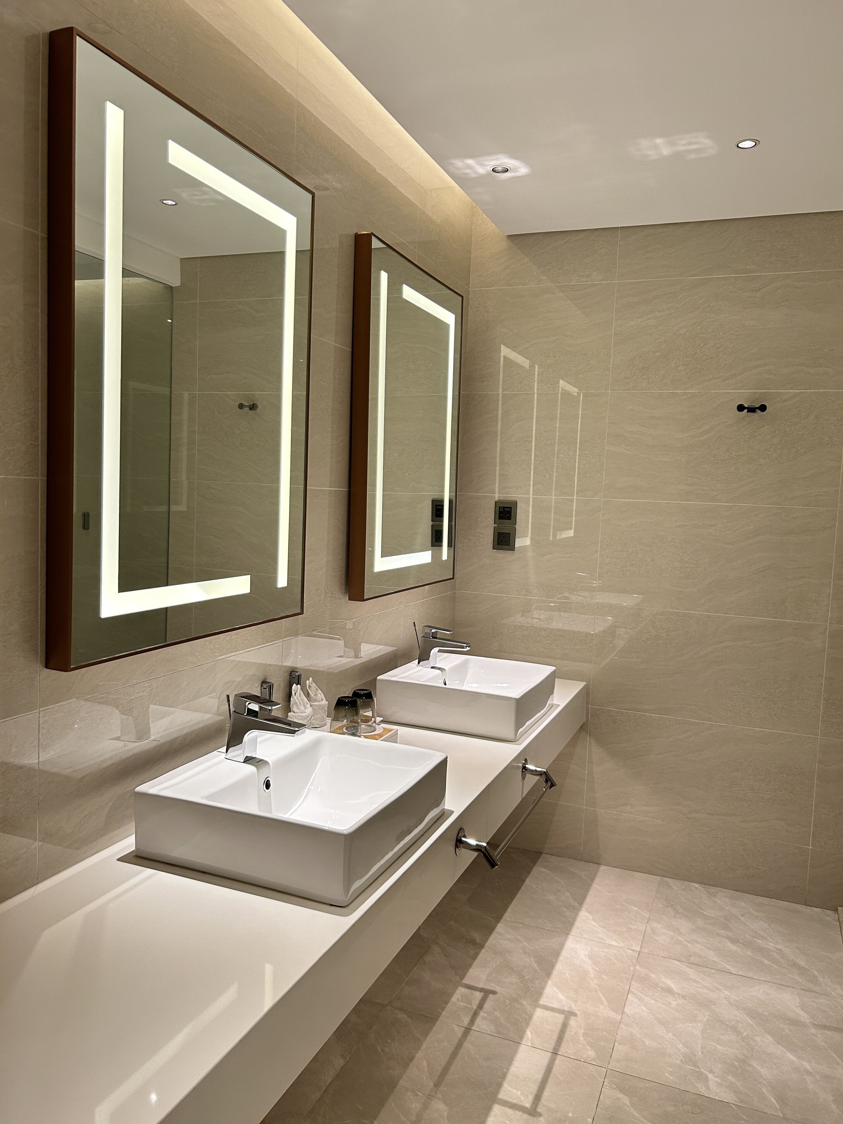 A modern bathroom with two sinks, large mirrors, and a wall-mounted towel dispenser.