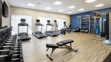 A gym with treadmills, elliptical machines, dumbbells, and a weight bench.