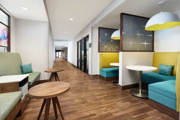 Un hall d’hôtel moderne, doté d’espaces aménagés avec des sièges, des tables rondes et des luminaires suspendus.