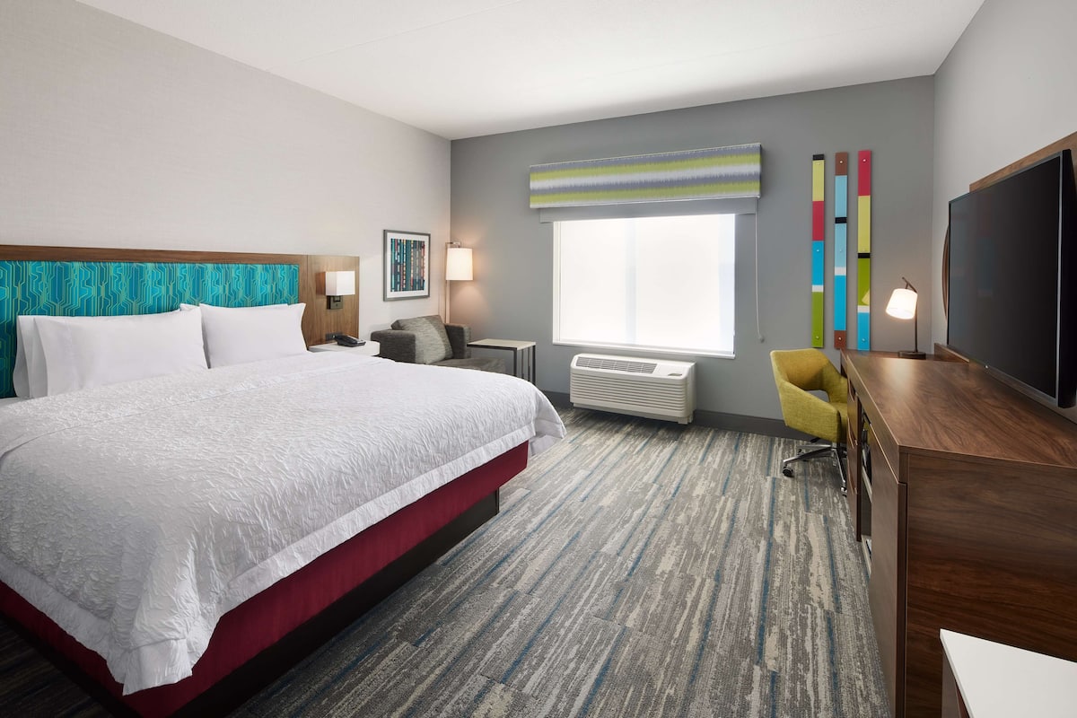 Habitación de hotel con una cama grande, un escritorio, una silla, un televisor, una ventana y aire acondicionado instalado en la pared.