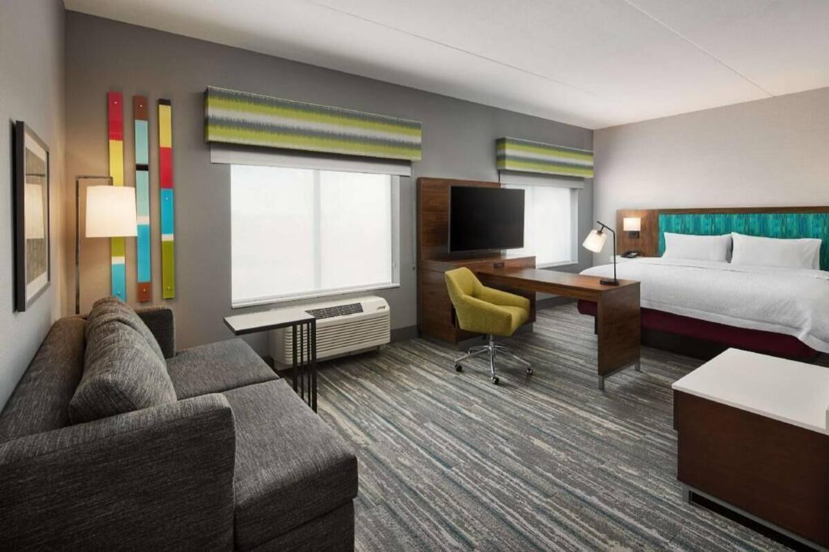 Habitación de hotel con sofá, escritorio, silla, cama, televisión y ventana.