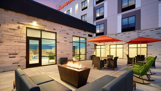 A hotel with a stone facade, outdoor seating area with fire feature, and umbrellas. - Hampton Inn & Suites Franklin Indianapolis (Franklin)
