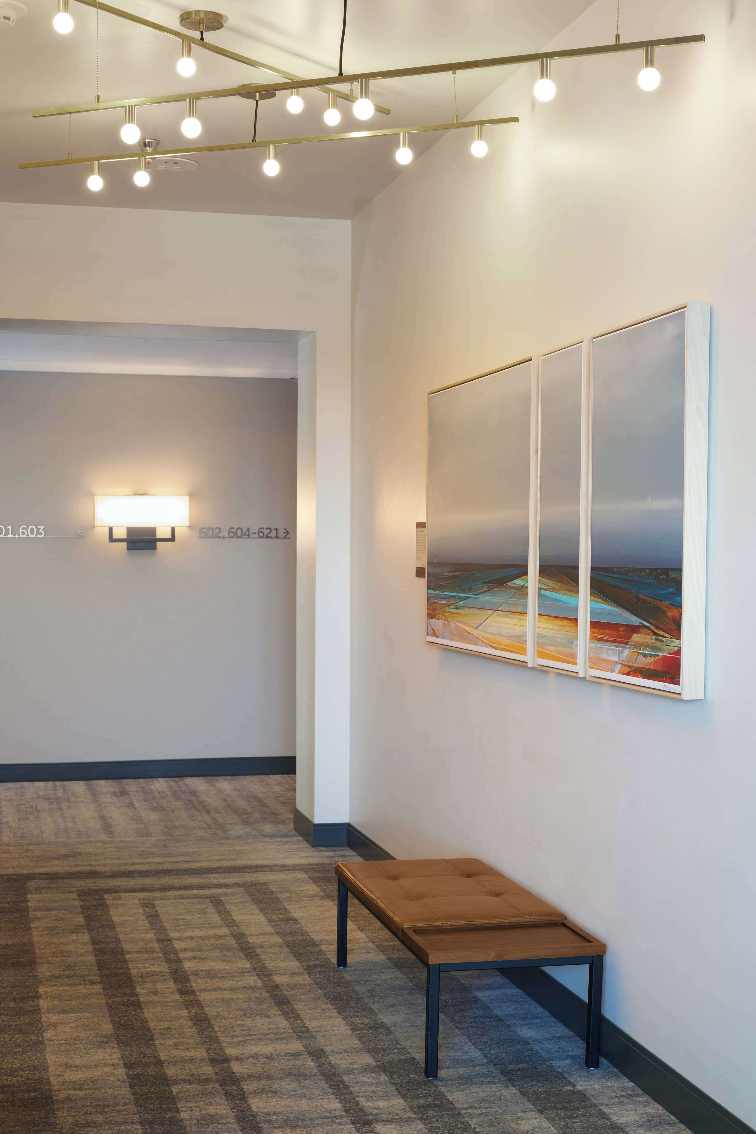 A hallway with a bench, a painting on the wall, and a light fixture.