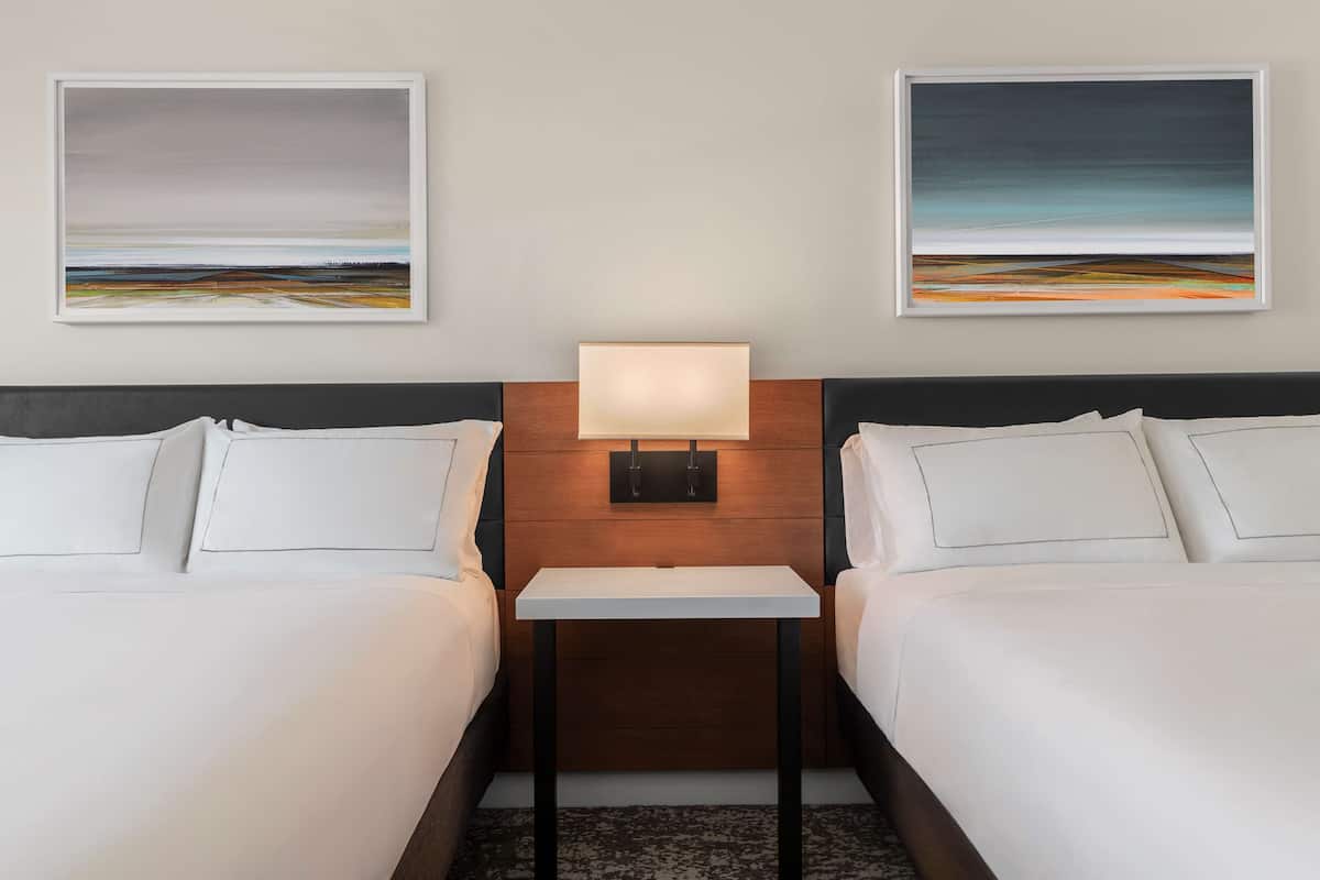 Een hotelkamer met twee bedden, een nachtkastje met een lamp en twee ingelijste kunstwerken aan de muur.