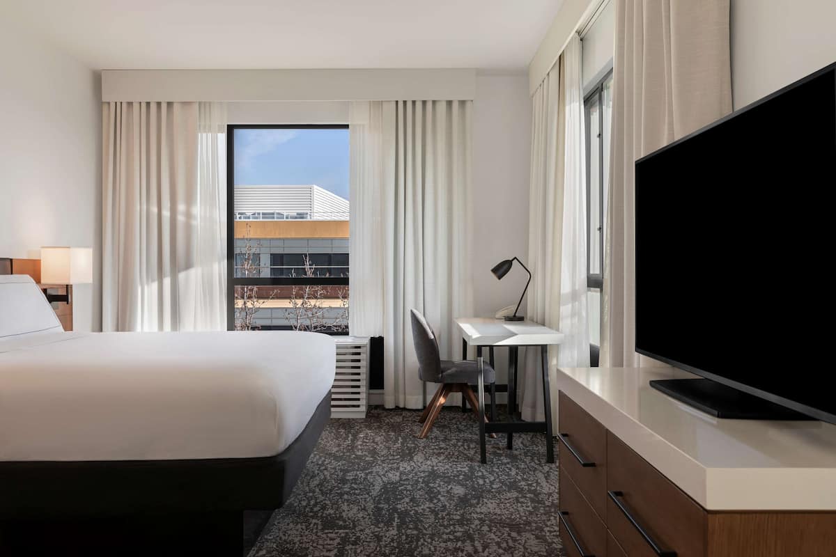 Een hotelkamer met een bed, een bureau, een stoel, een televisie en een raam met gordijnen.