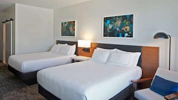 Quarto de hotel com duas camas, uma cadeira, um abajur e duas pinturas na parede.