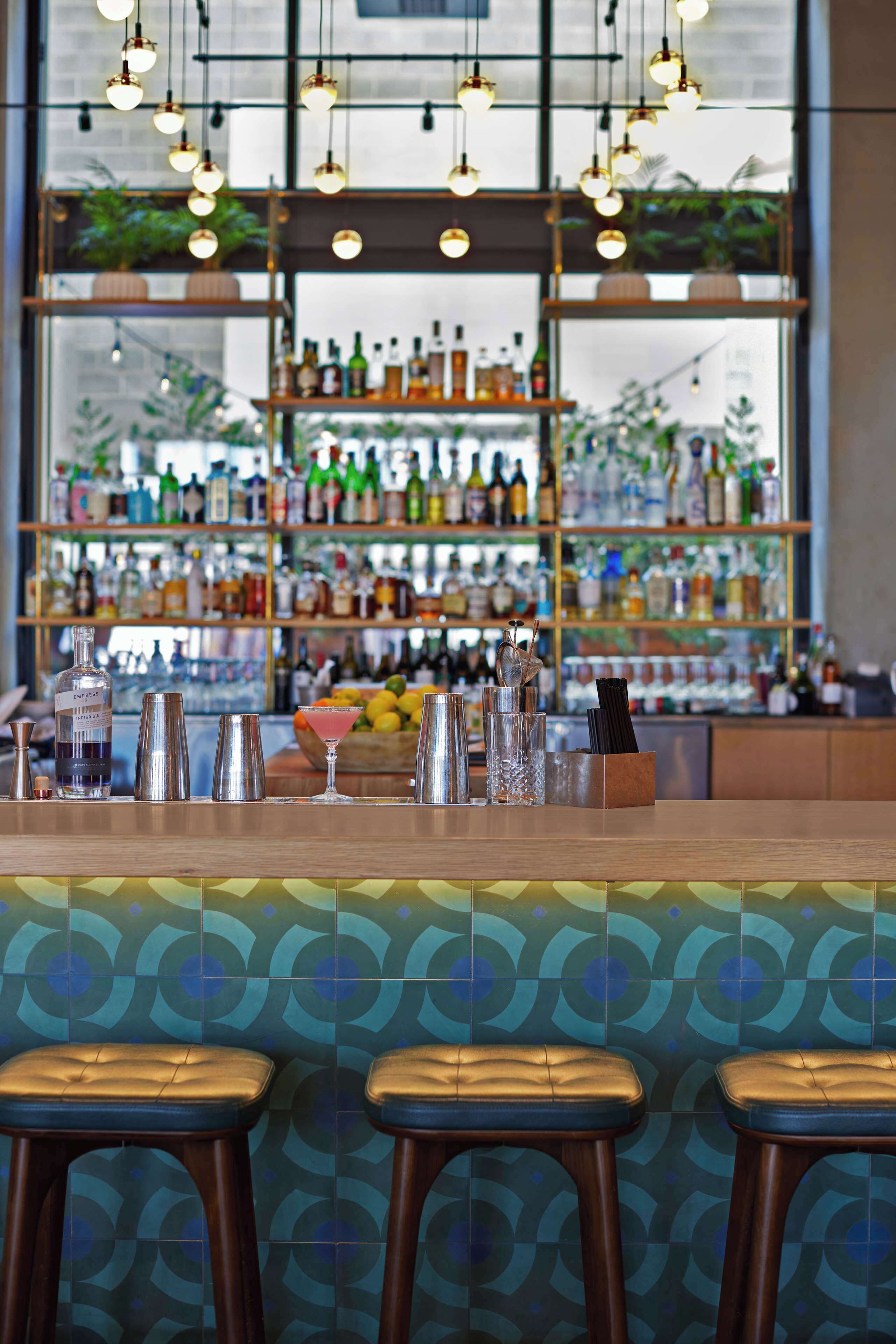 Zona de bar con taburetes, barra y estanterías llenas de botellas.