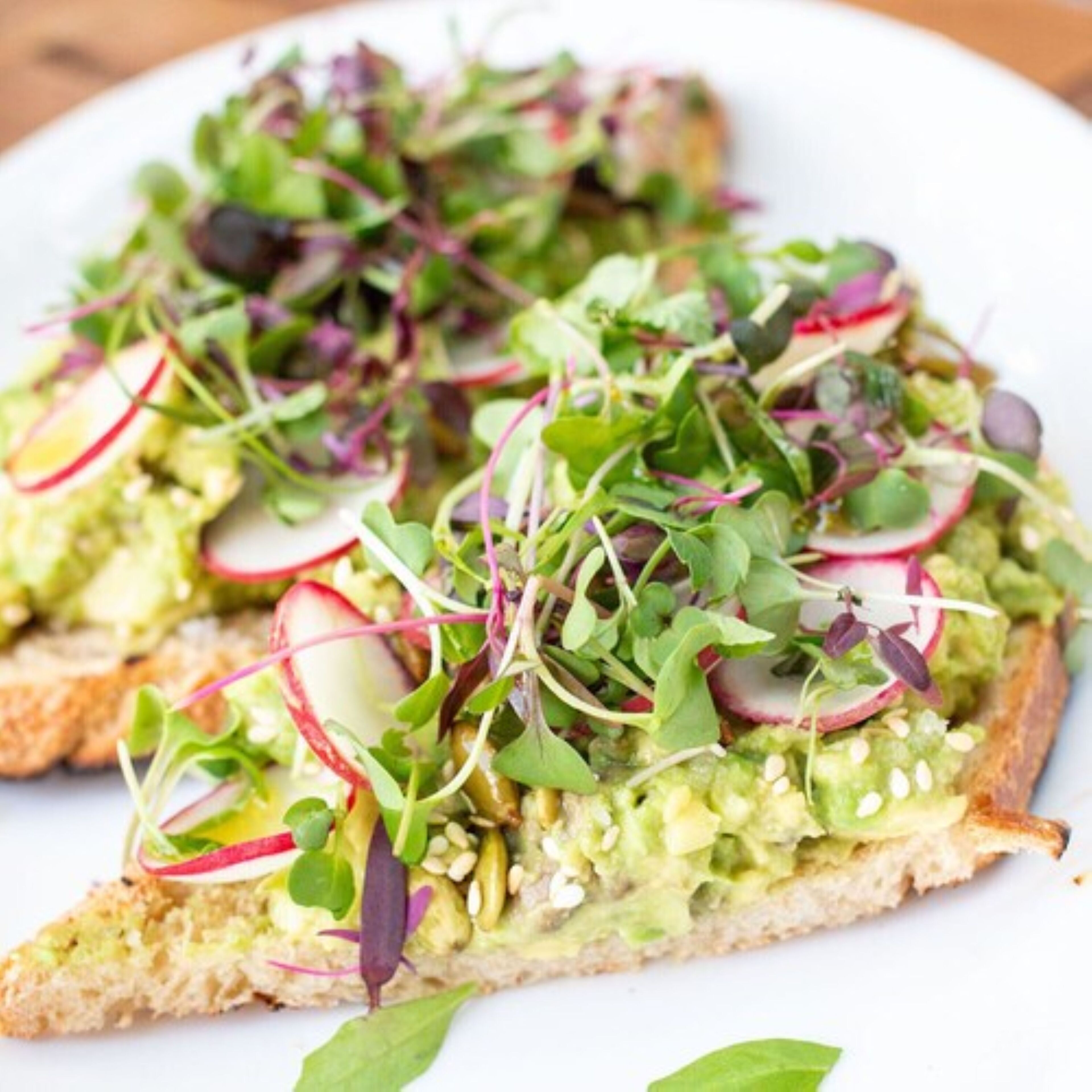 A plate of avocado toast topped with radishes and sprouts.