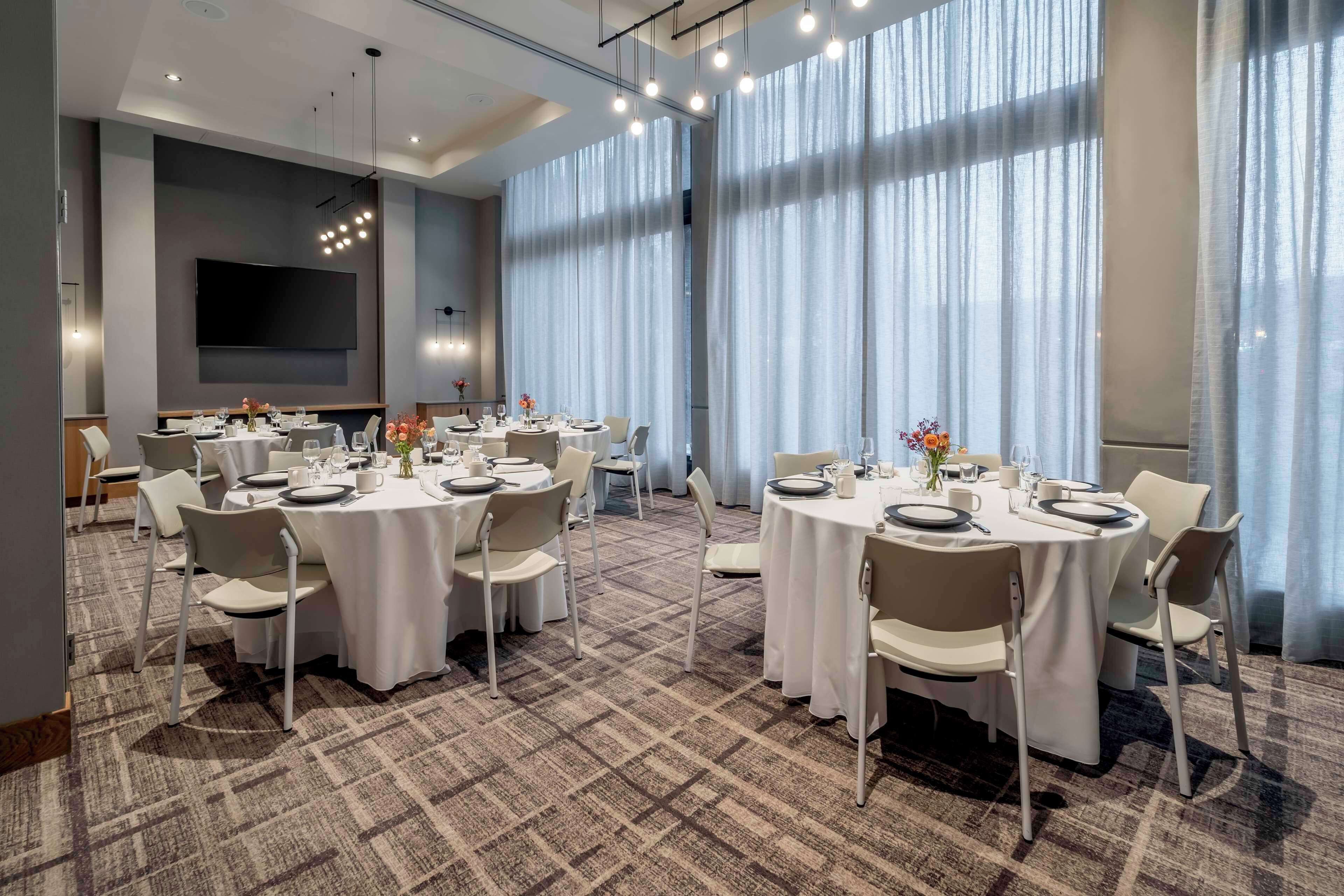 A conference room with round tables, white chairs, and a large screen.