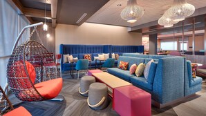 Ein stilvoller Lounge-Bereich mit einem blauen Sofa, farbenfrohen Kissen, einem Hängesessel und einer Holzbank.
