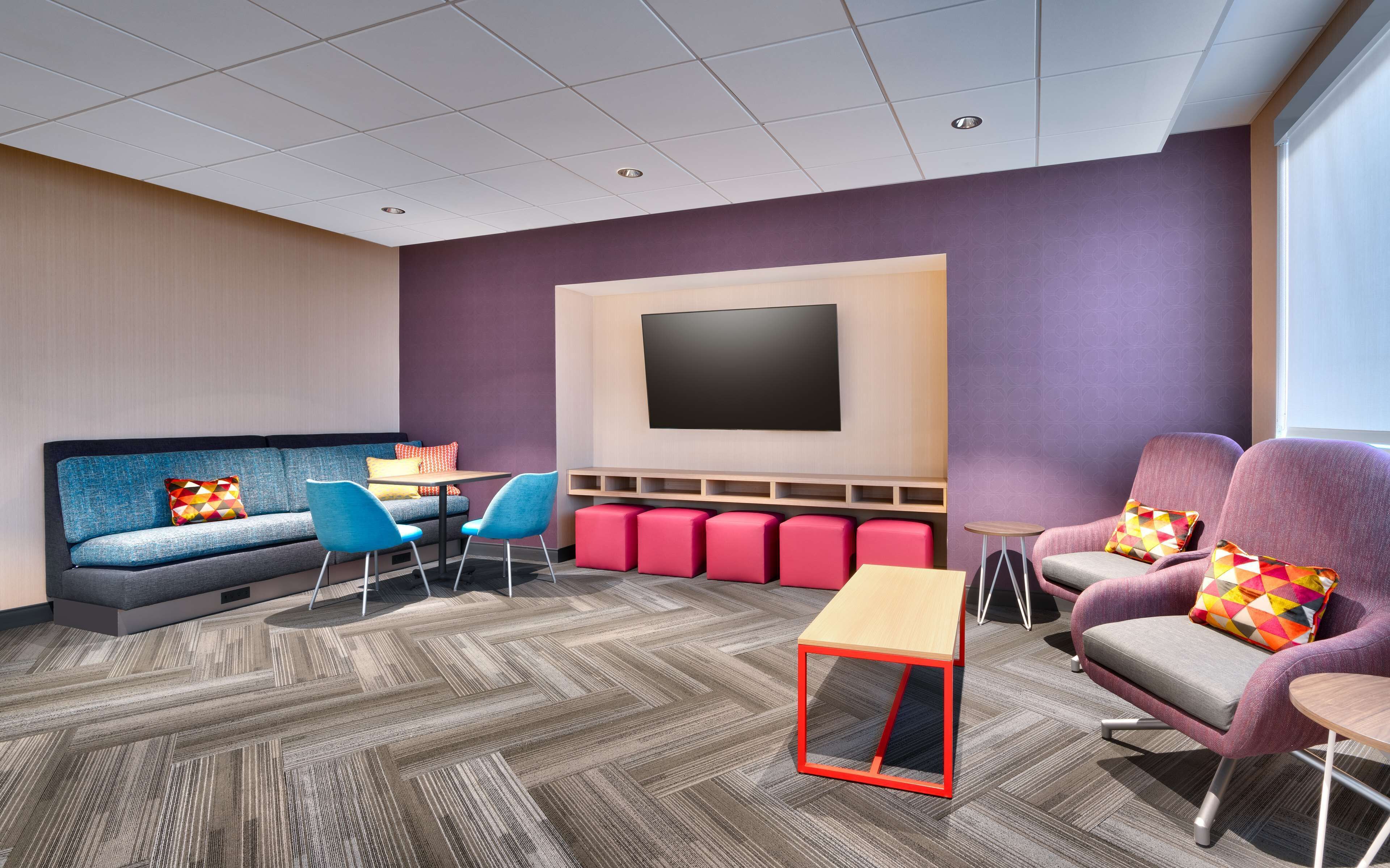 Un'area lounge moderna con un ampio televisore a schermo piatto, sedute confortevoli e un tappeto a motivi a spina di pesce.