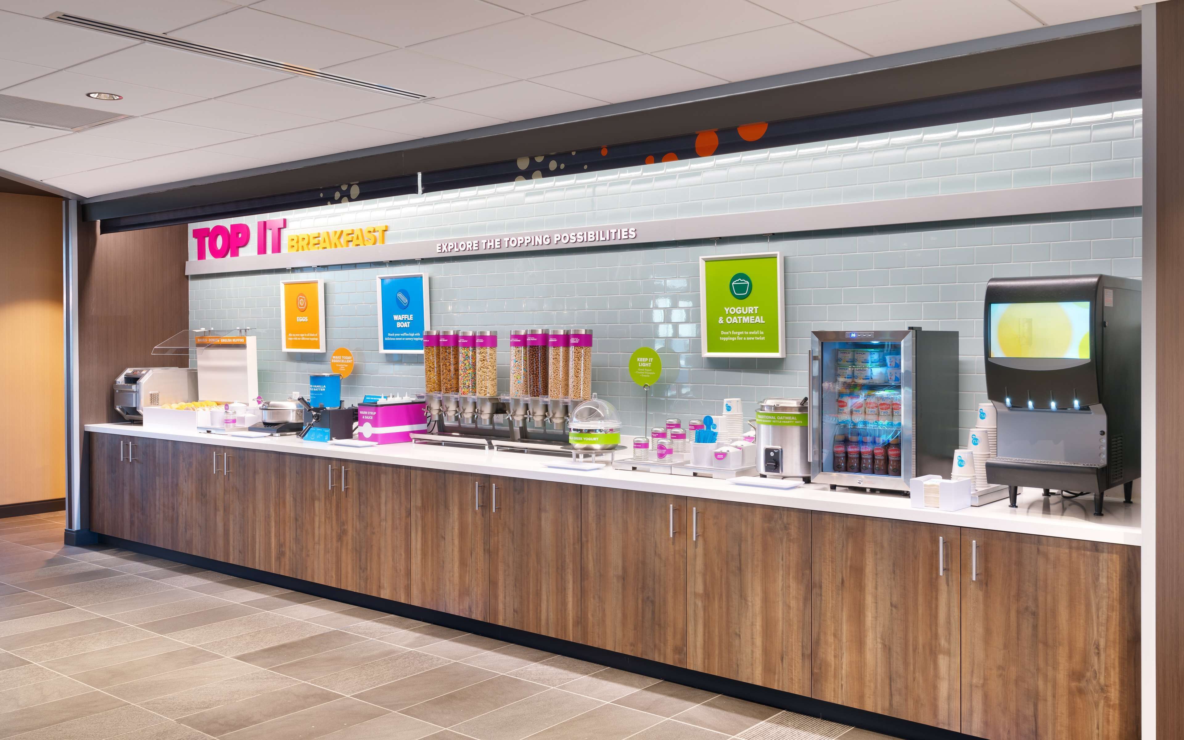 A breakfast counter with a sign reading "TOP IT BREAKFAST" and various food options like waffles and yogurt.