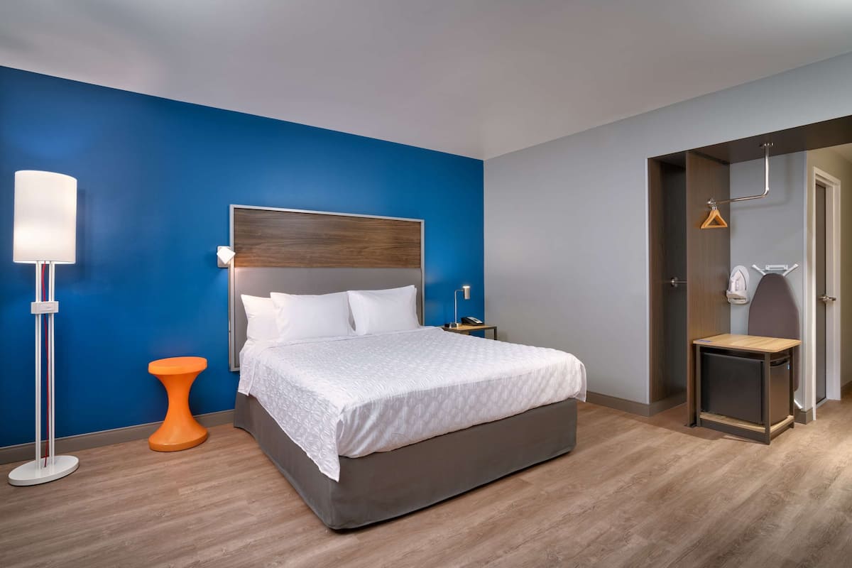 Een moderne hotelkamer met een groot bed, een nachtkastje, een vloerlamp en een strijkplank.