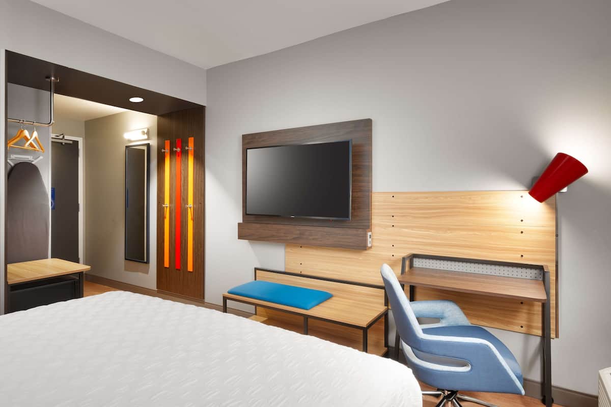 Een hotelkamer met een bed, een bureau, een stoel, een televisie en een kledingkast.