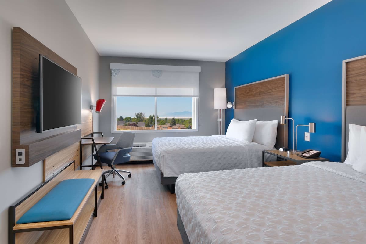 Een hotelkamer met twee bedden, een bureau met stoel, een televisie en een raam met uitzicht.