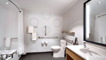 Un baño moderno con inodoro, bidé y lavamanos. Hay barras de apoyo, un perchero para toallas y un espejo.
