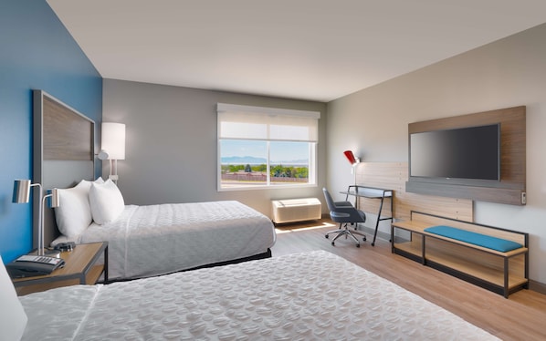 A modern hotel room with a large bed, a desk with a chair, a TV mounted on the wall, and a window with a view of the city.