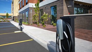 A modern building with a parking lot and electric vehicle charging stations. - Home2 Suites by Hilton Utica, NY (Utica)