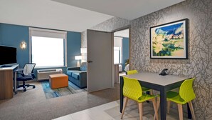 A modern hotel room with a desk, office chair, and a dining area with a table and chairs. - Home2 Suites by Hilton Utica, NY (Utica)