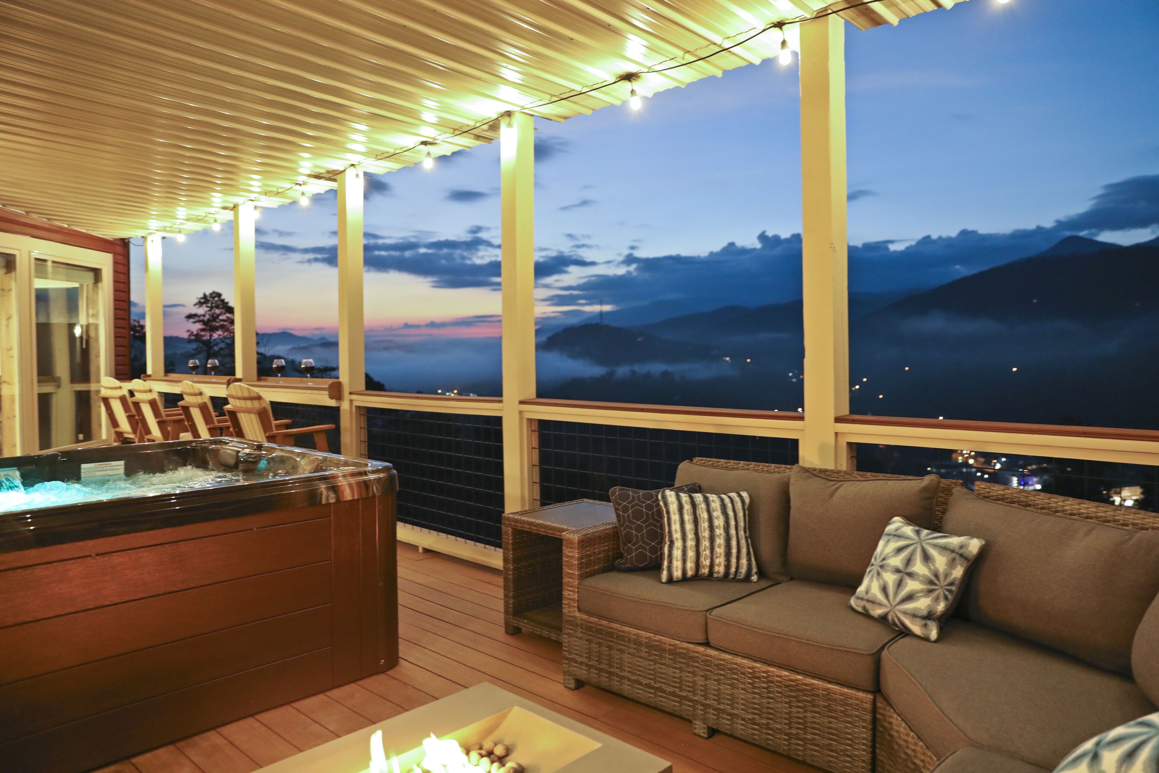 A hot tub, wicker sofa, and a view of mountains at dusk.