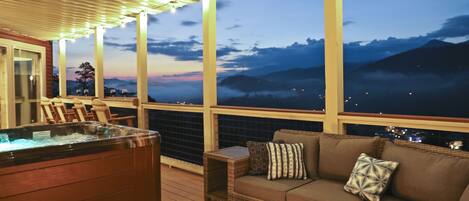 A hot tub, wicker sofa, and a view of mountains at dusk.