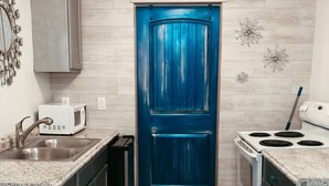Une cuisine de taille réduite avec une porte bleue, des appareils en acier inoxydable et un revêtement de sol en bois clair.