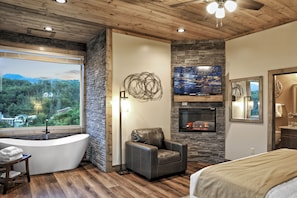 Une salle de bain moderne avec une baignoire sur pieds, un mur d’accent en pierre, une cheminée et une grande fenêtre donnant sur une zone boisée.