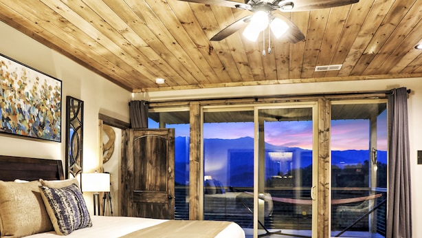 A bedroom with a large bed, wooden ceiling, and a view of mountains through glass doors.
