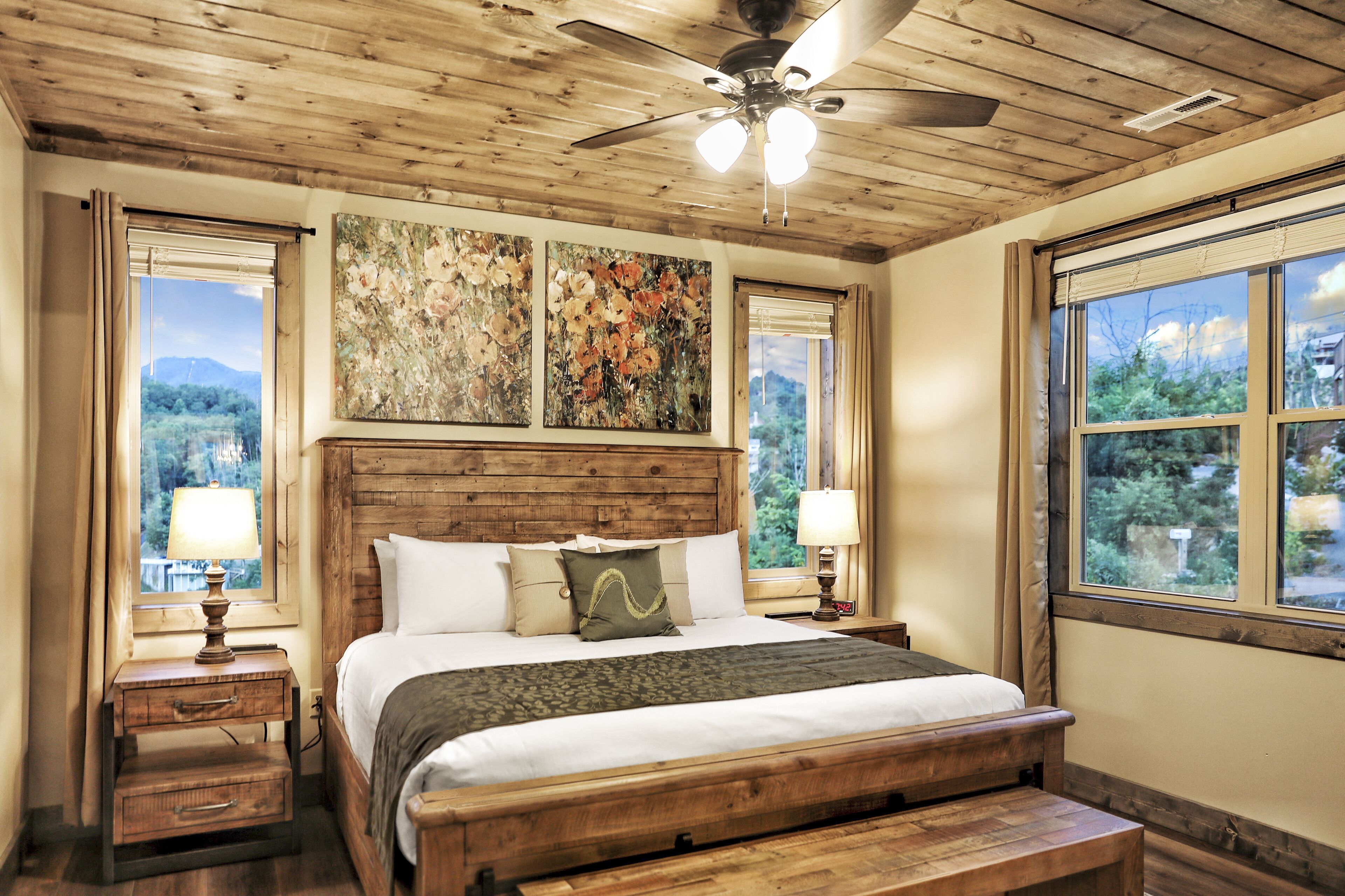 A bedroom with a wooden headboard, a large bed, two bedside tables with lamps, and a ceiling fan.