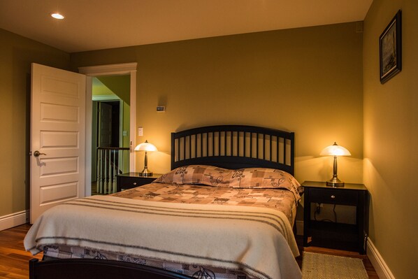A bedroom with a bed, two bedside tables with lamps, a door, and a hallway.