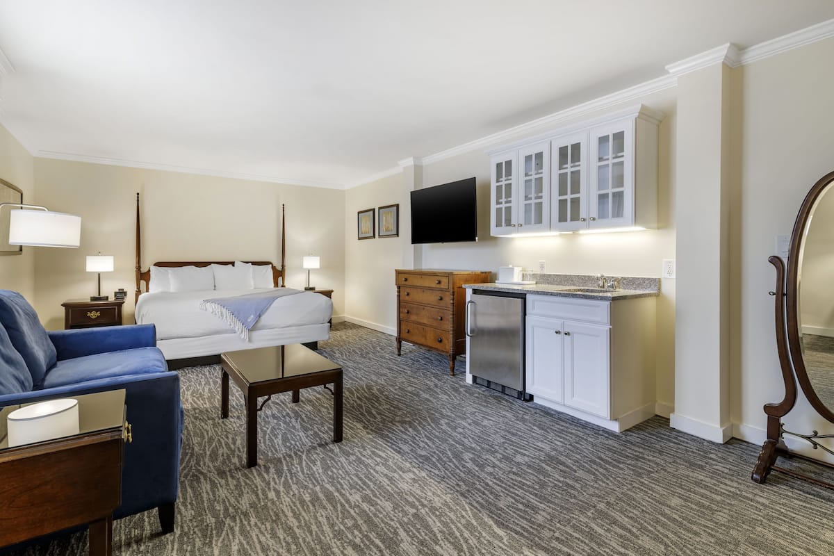 Habitación de hotel con cama, sofá, una mesita, escritorio, kitchenette y televisor montado en la pared.