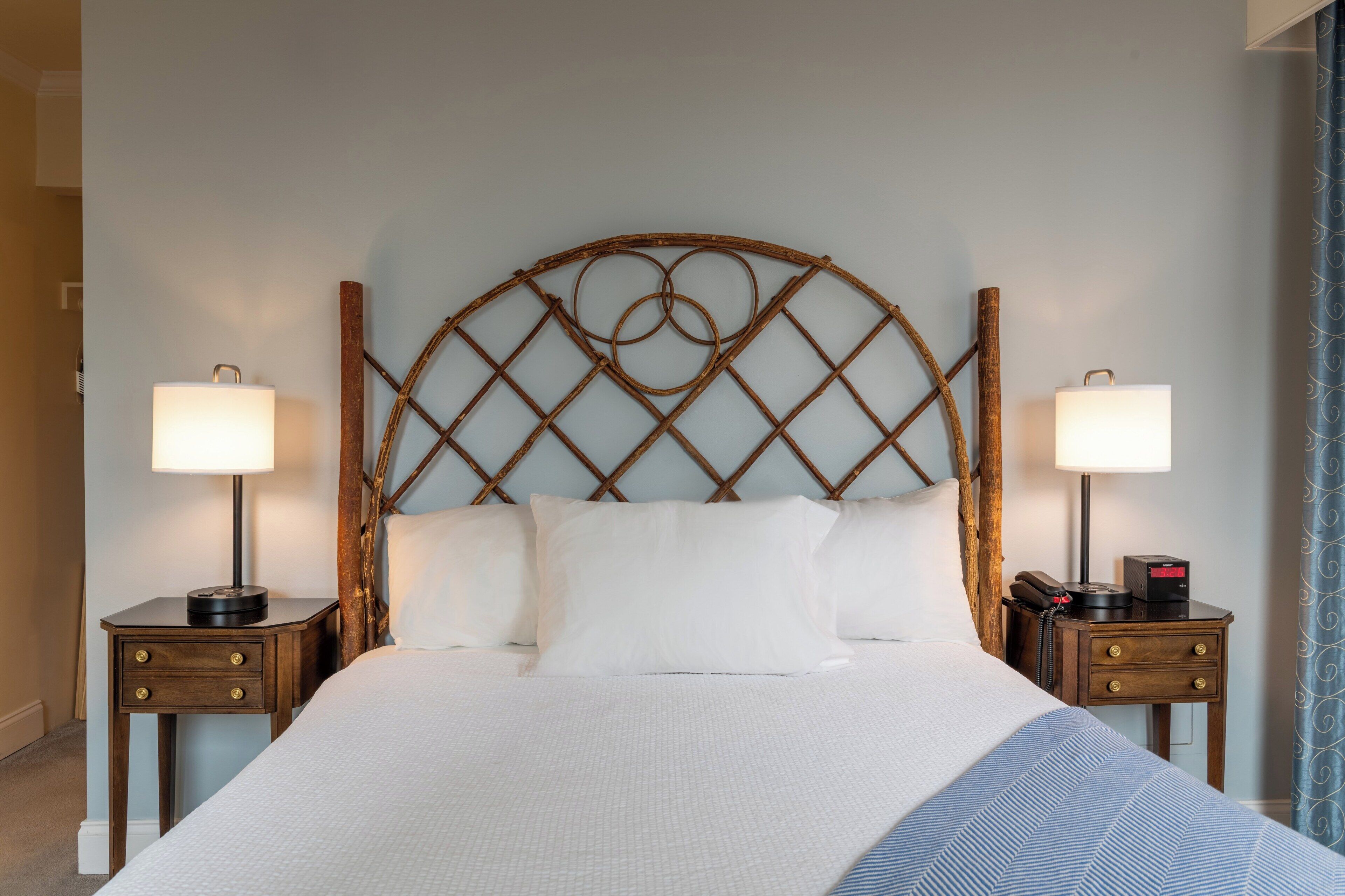 A neatly made bed with white bedding, two bedside tables with lamps, and a wooden headboard with a circular design.