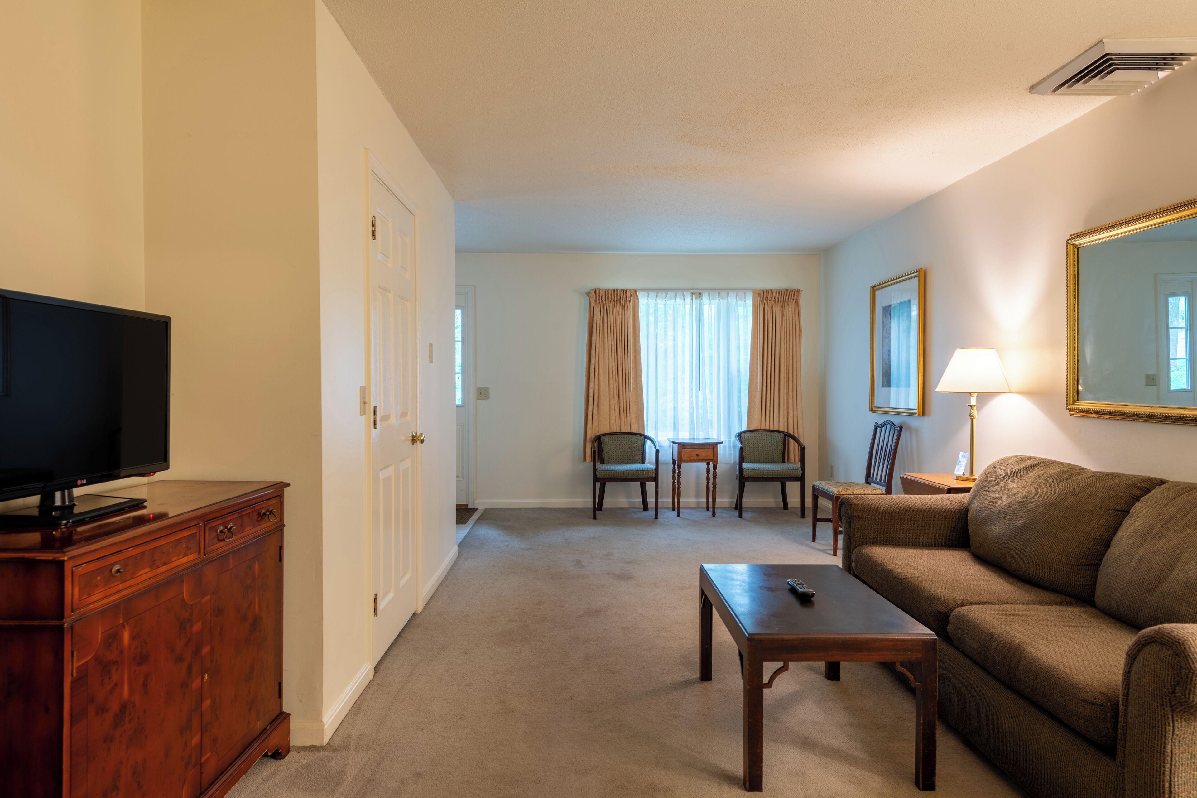 A hotel room with a television, wooden dresser, brown sofa, and a small table.