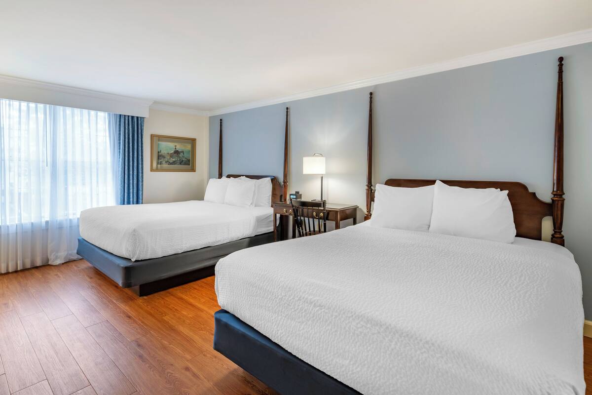 Una habitación de hotel con dos camas, cabeceros de madera, una mesita de noche, una lámpara y un cuadro en la pared.