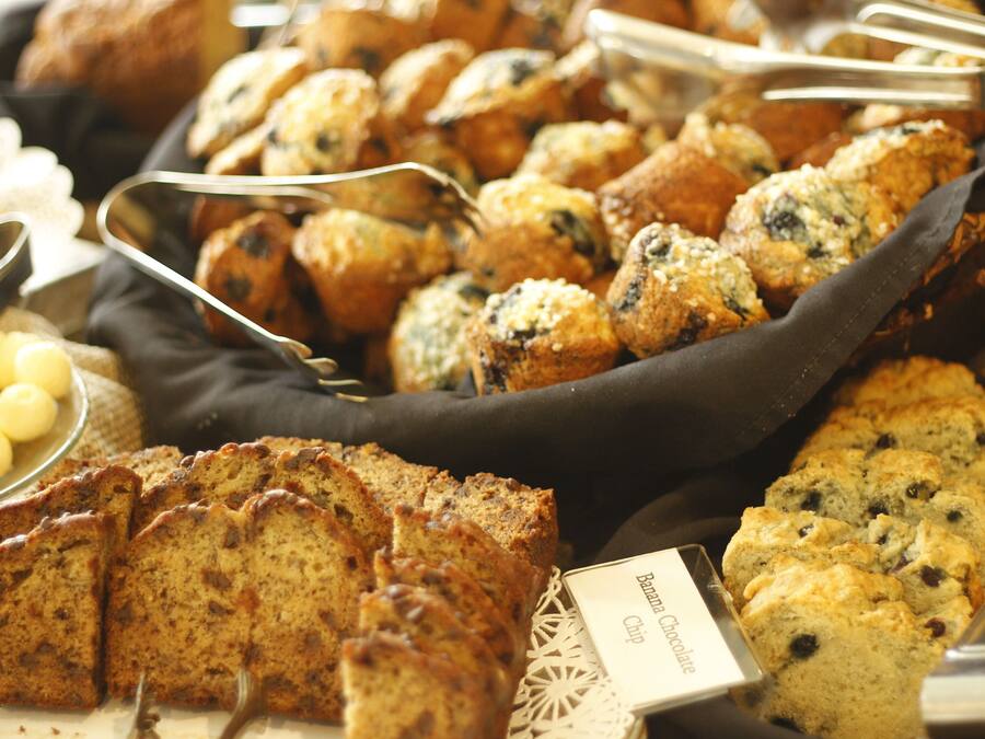 Variedad de productos horneados, como muffins y pan, dispuestos en una bandeja con una etiqueta que dice 'Banana Chocolate Chip'.