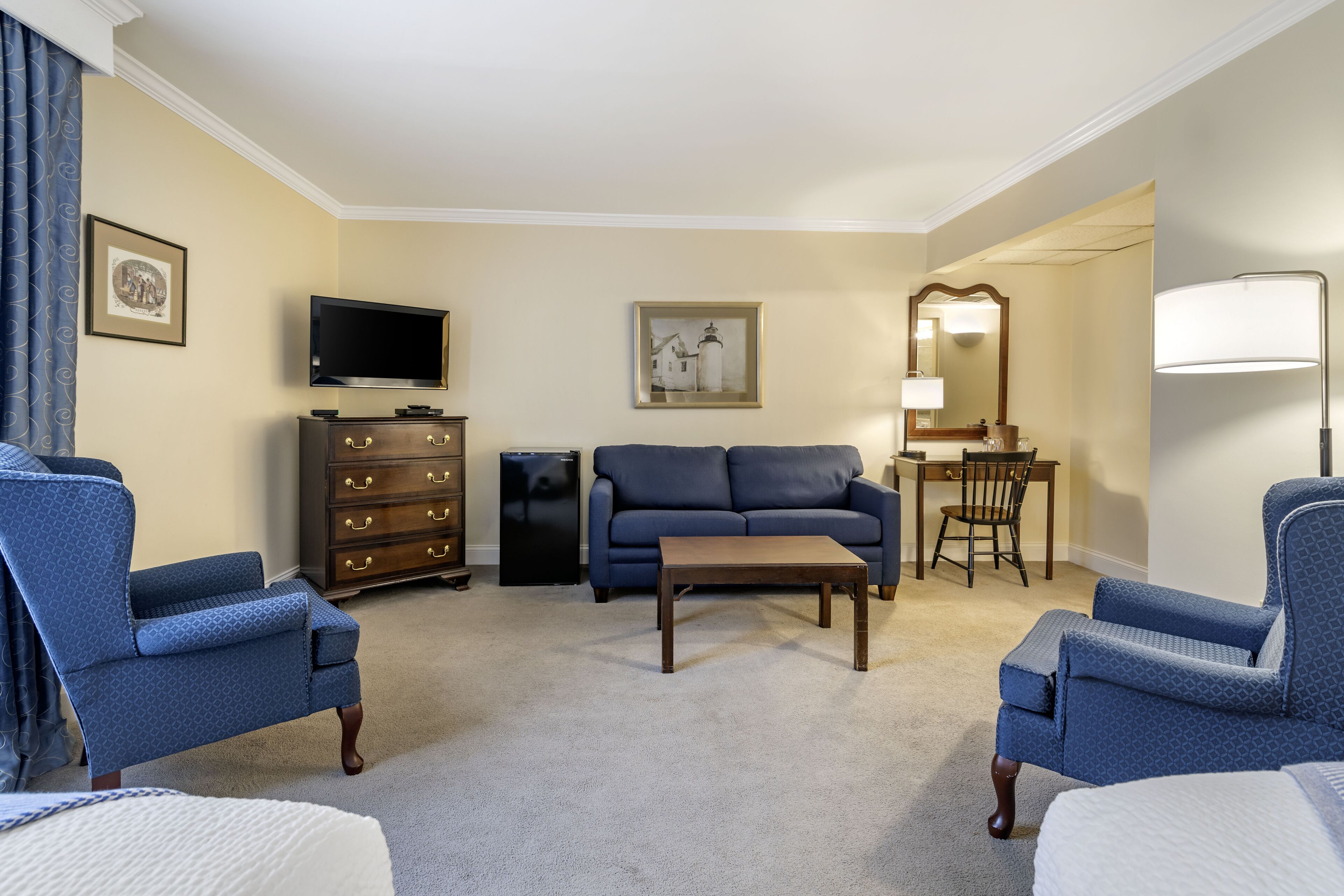 A hotel room with a sofa, two armchairs, a coffee table, a TV, a dresser, and a desk with a chair.