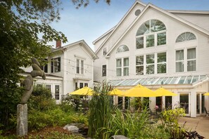 A two-story building with a large glass conservatory and yellow umbrellas in the garden area. - The Harraseeket Inn & Event House Freeport Downtown (Freeport)