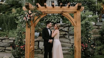 A wooden arbor with floral decorations, set against a stone wall and lush greenery.