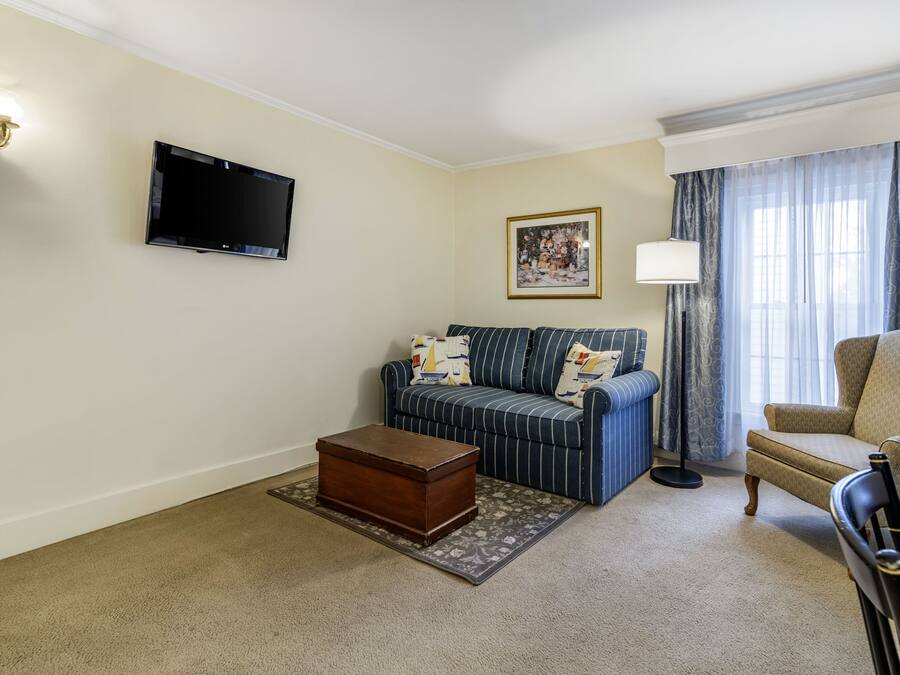 A living room with a sofa, armchair, wooden chest, and a flat-screen TV.