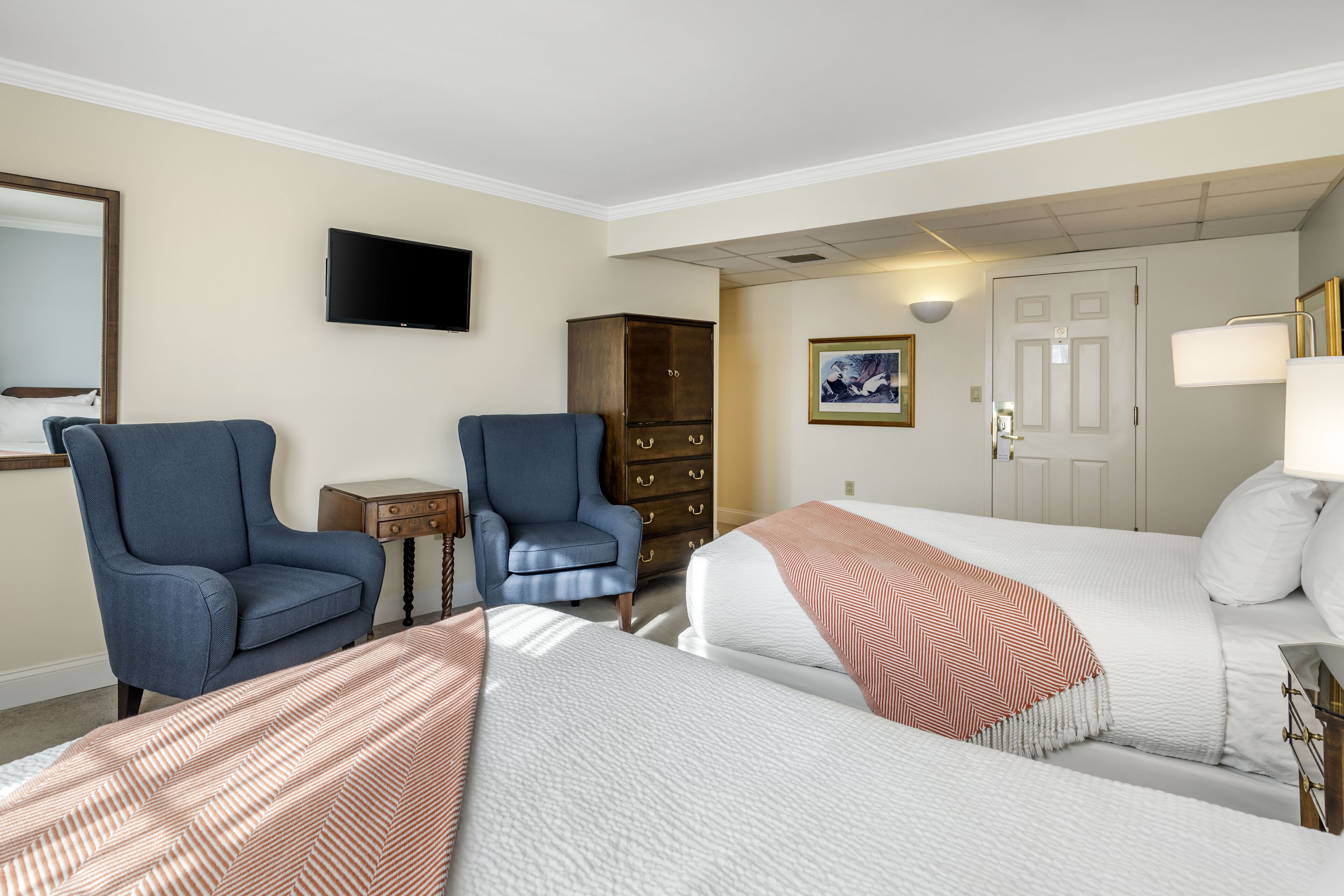 Une chambre d’hôtel avec deux lits, une télévision, une armoire et un bureau avec une lampe.